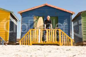 Portrait of man standing with surfboard at beach hut