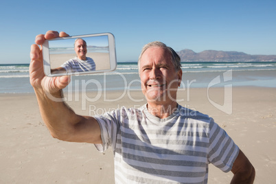 Smiling senior man holding smart phone while standing against sea