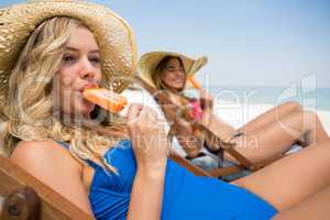 Female friends eating popsicles while relaxing on desk chair