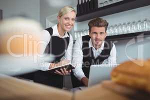 Smiling waiters using laptop at counter in restaurant