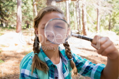 Girl looking through magnifying glass in the forest