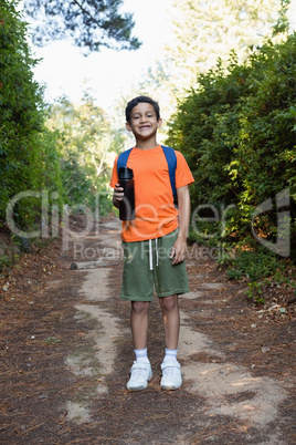 Boy with backpack and water bottle standing on the path in forest