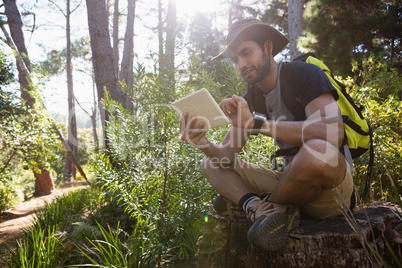 Man using digital tablet while resting on the tree stump