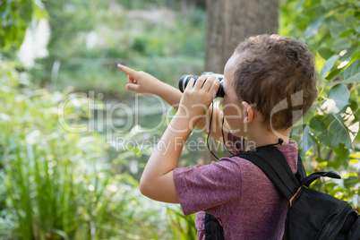 Boy looking through binoculars and pointing in the forest