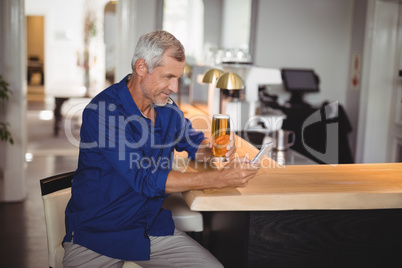 Mature man using mobile phone while having beer