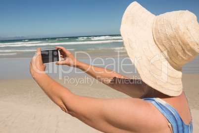 Side view of woman holding mobile phone while standing at beach