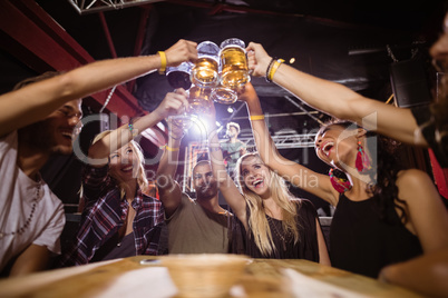 Low angle view of happy friends toasting beer glasses while sitting at table