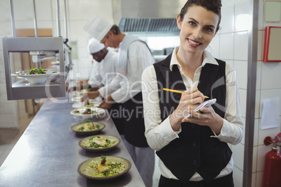 Smiling waitress with note pad in commercial kitchen