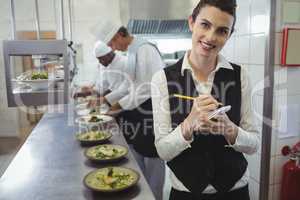 Smiling waitress with note pad in commercial kitchen