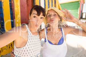 Portrait of cheerful mother and daughter puckering while standing against hut