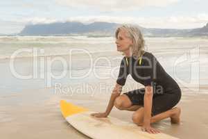 Senior woman kneeling by surfboard on shore