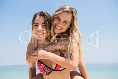 Portrait of cheerful woman piggybacking female friend against clear sky