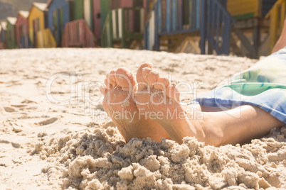Low section of woman sitting on sand against beach huts