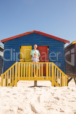 Portrait of smiling boy with grandfather standing at beach hut
