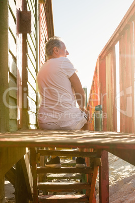 Rear view of man sitting on steps of hut against clear sky
