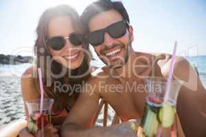 Portrait of happy couple holding drinks at beach