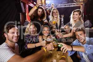Portrait of cheerful friends toasting drink at table with performer singing on stage