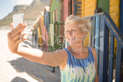 Happy senior woman clicking selfie while standing against beach hut