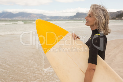 Side view of smiling woman carrying surfboard while standing on shore