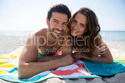 Portrait of smiling young couple lying together on blanket at beach