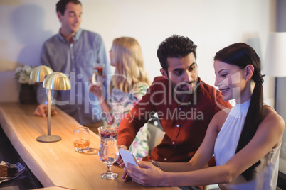 Couple interacting with each other while using mobile phone at bar counter