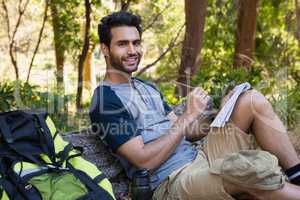 Smiling man writing on notepad while resting on tree trunk