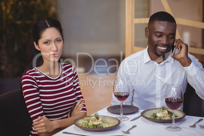 Man ignoring bored woman while talking on mobile phone