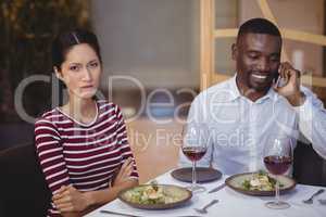 Man ignoring bored woman while talking on mobile phone