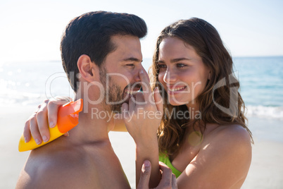 Smiling young woman applying sunscream on man nose at beach