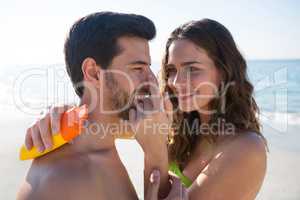 Smiling young woman applying sunscream on man nose at beach