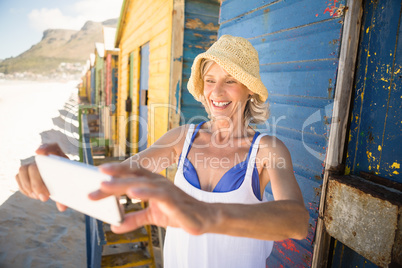 Smiling woman holding mobile phone while standing against wall