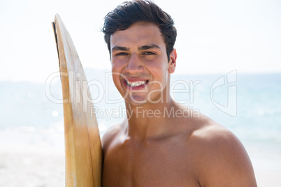 Portrait of smiling young man holding surfboard at beach