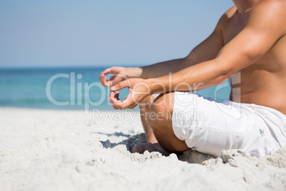 Low section of shirtless man meditating at beach