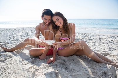 Smiling young couple taking selfie while sitting at beach