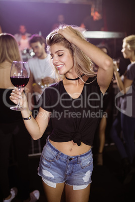 Smiling young woman holding wineglass while dancing at nightclub