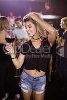 Smiling young woman holding wineglass while dancing at nightclub