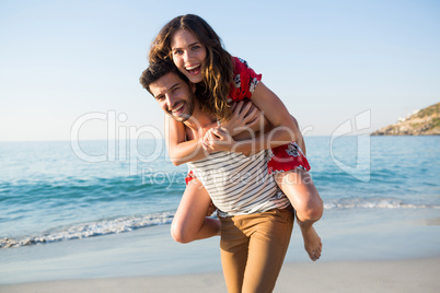 Portrait of young man piggybacking his cheerful girlfriend at beach
