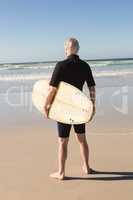 Rear view of senior man with surfboard standing on sand