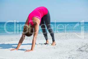Woman bending on sand while exercising at beach