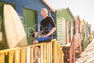 Senior man looking away while sitting on railing of hut