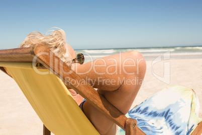 Side view of senior woman relaxing on chair against clear sky