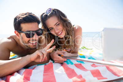 Smiling couple taking selfie while lying together on blanket at beach