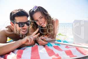 Smiling couple taking selfie while lying together on blanket at beach