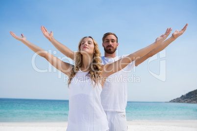 Couple with arms outstretched exercising at beach