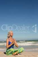 Close up of woman meditating while sitting on shore against clear sky