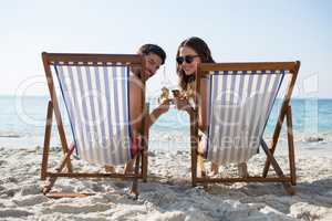 Portrait of couple holding drinks while relaxing on deck chairs at beach