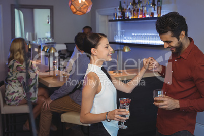 Couple holding glass of drink while dancing in bar restaurant