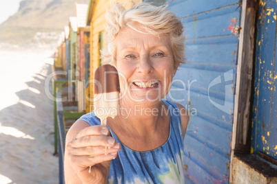 Portrait of happy senior woman holding ice cream while standing by hut