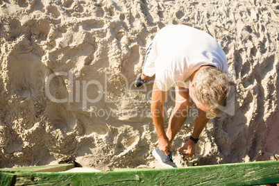 High angle view of senior man tying shoelace while standing on sand