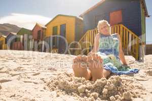 Woman relaxing on sand against huts at beach